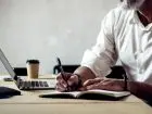 Elegancko ubrany mężczyzna piszący w notatniku i używający laptopa